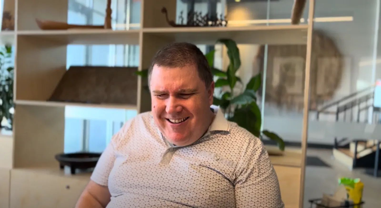 A male in a white shirt is smiling in an office environment.