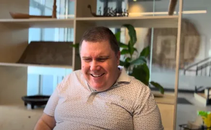 A male in a white shirt is smiling in an office environment.