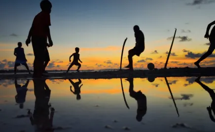 Silhouettes of young people playing a ball game on the beach at sunset.