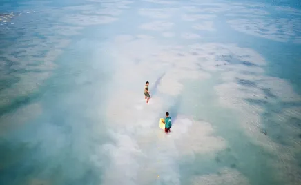 Aerial drone shot of two small figures are fishing with nets in crystal blue shallow water.