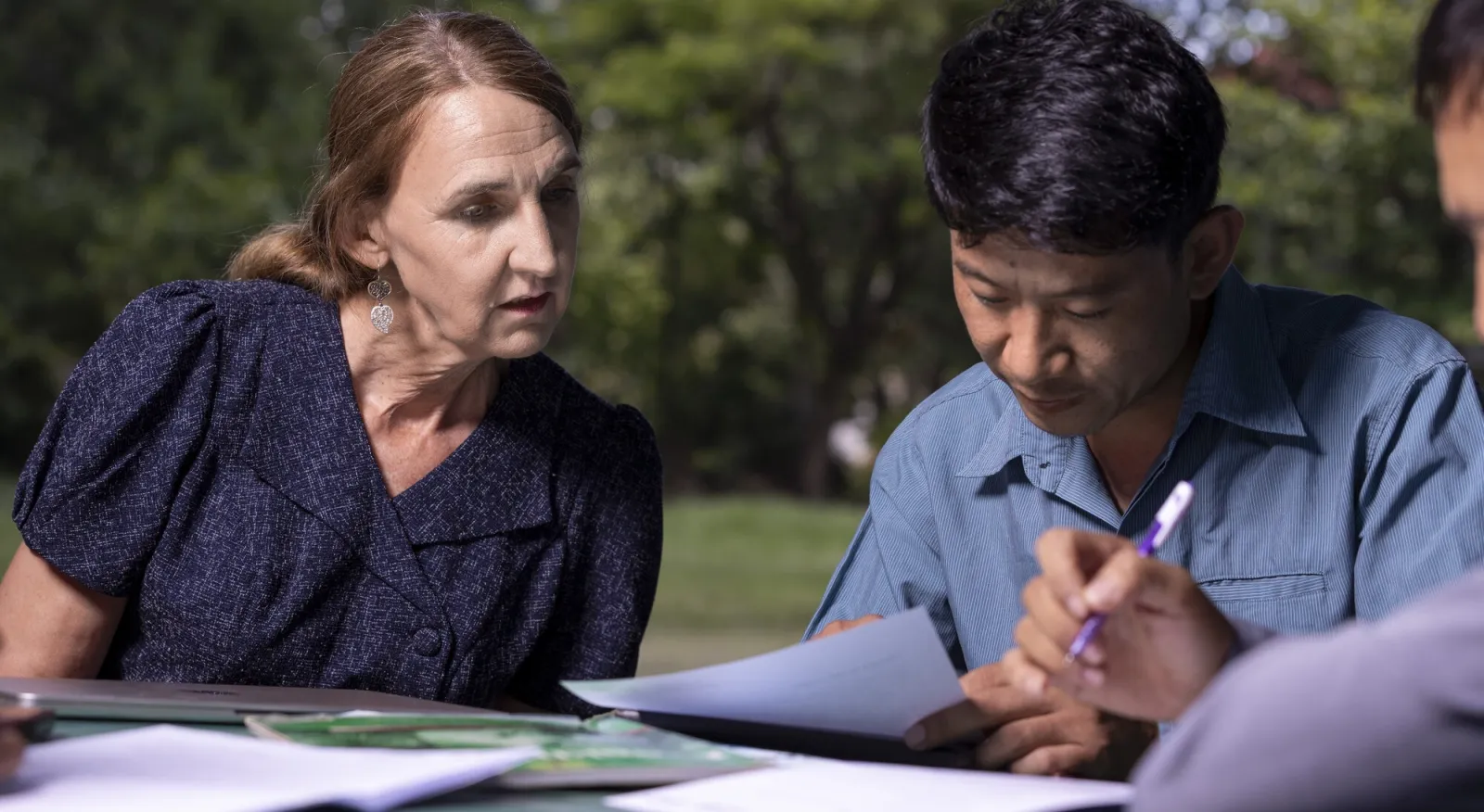 A lady, Lorise, and a man, Chanthaluck, look at a book together, they are mid-discussion
