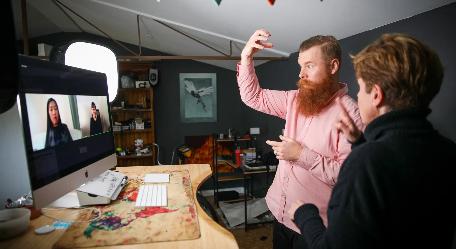Two people are on the screen and two people are standing in an office using sign language to communicate.
