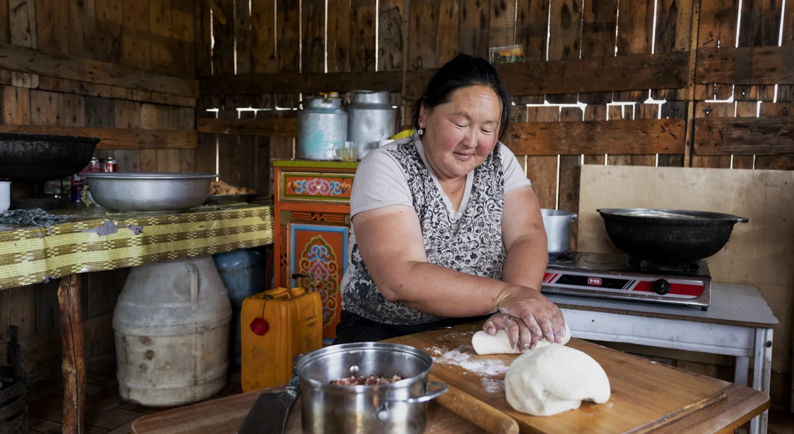A person is rolling dough in a traditional Mongolian kitchen.