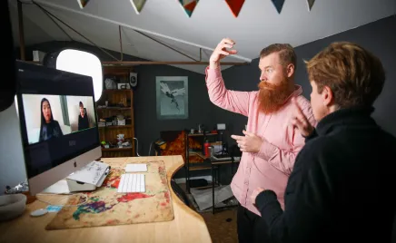 Two people are on the screen and two people are standing in an office using sign language to communicate.
