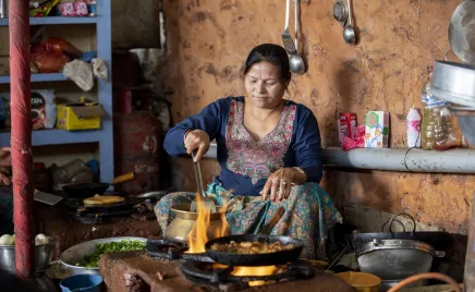 A woman sits next to an open stove preparing food.