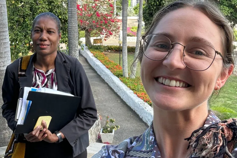 Two women smiling for a selfie outside, in front of their work office.