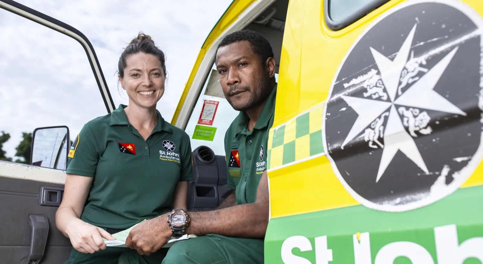 A man and a woman smile at a camera while sitting in an ambulance