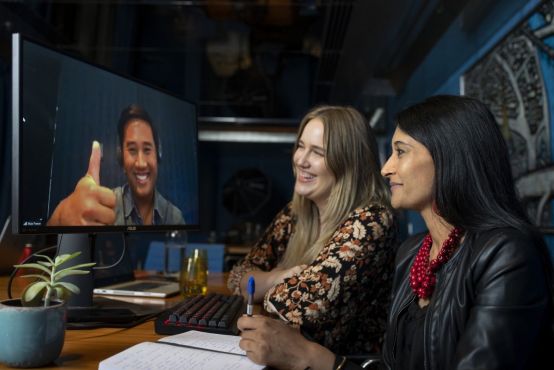 One man on a video call with two women sitting at a desk.