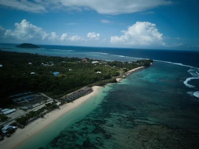 An aerial view of a beach, pristine waters, buildings and trees.