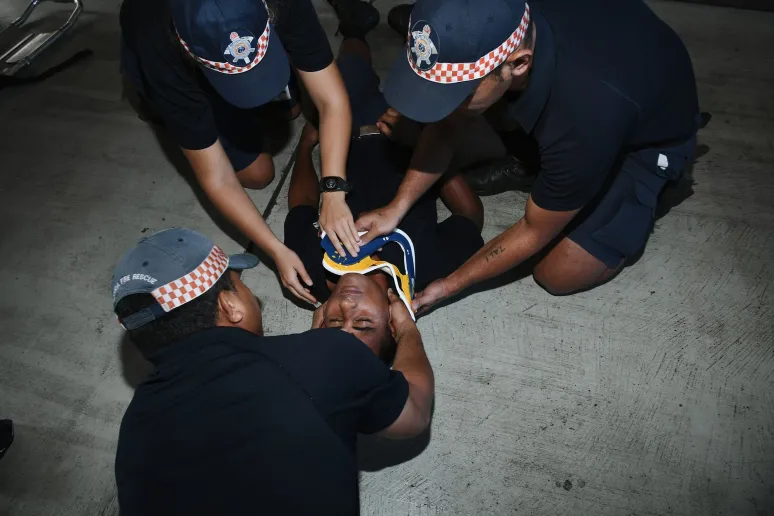 Three people assessing a person lying on the ground. They are all wearing emergency services uniforms.