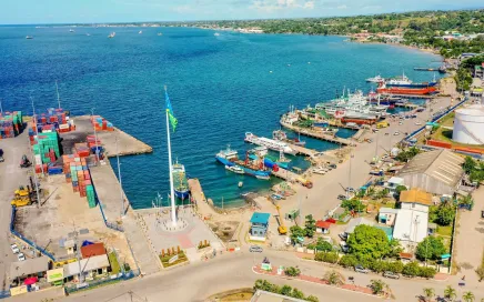 A busy port with crates and boats and a bright blue sea.