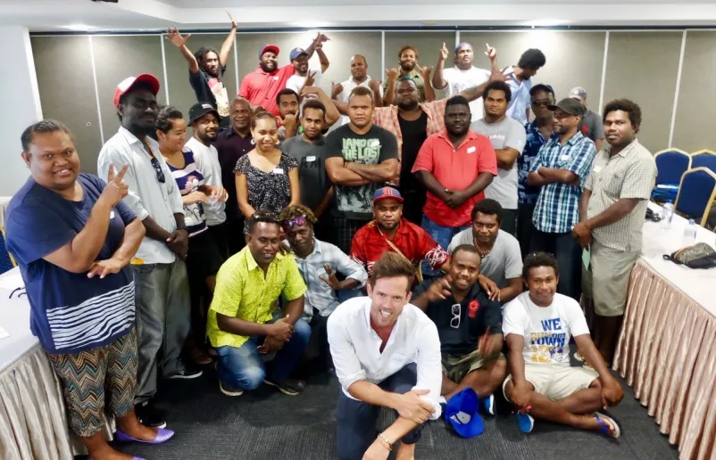 A group of people inside a room, some kneeling/sitting and others standing.