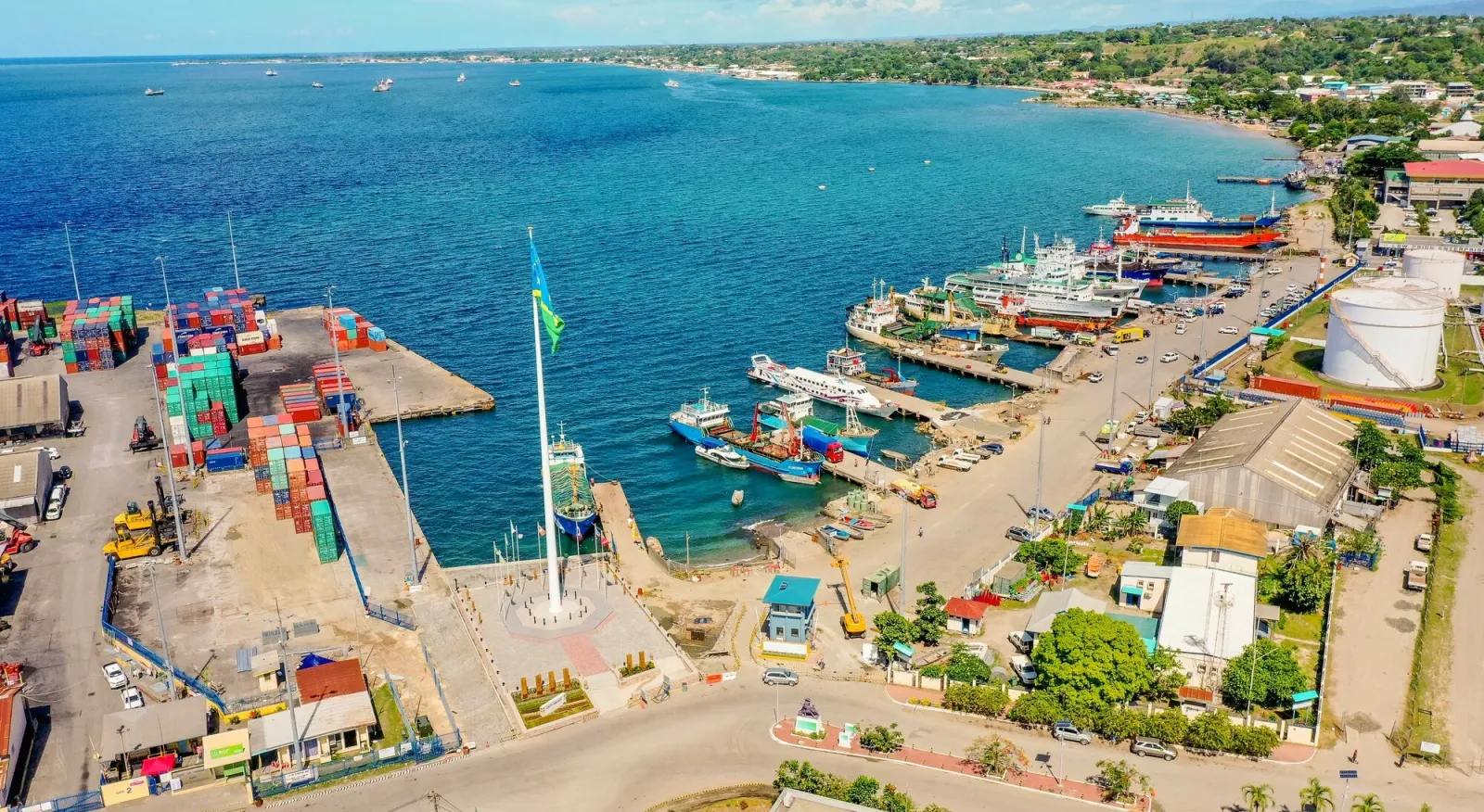 A busy port with crates and boats and a bright blue sea.