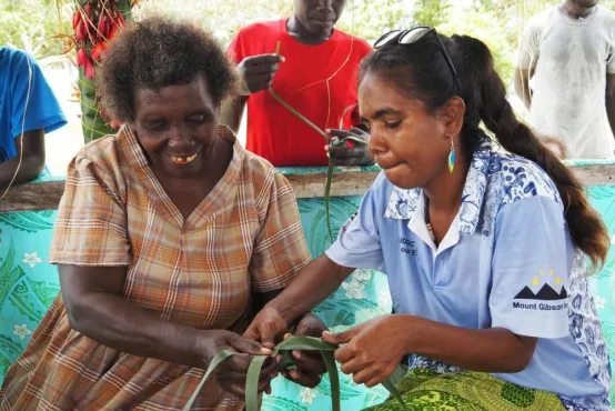 Two people are sitting together, weaving leaves