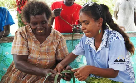 Two people are sitting together, weaving leaves