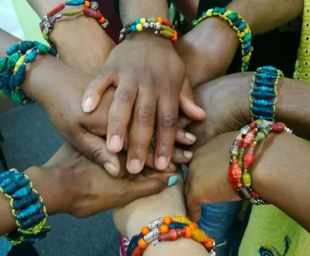 The hands of a group of diverse people wearing vibrant coloured bracelets.