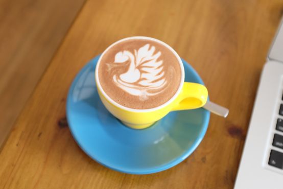 A cup of coffee with impressive latte art next to the edge of a laptop