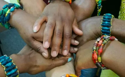 The hands of a group of diverse people wearing vibrant coloured bracelets.