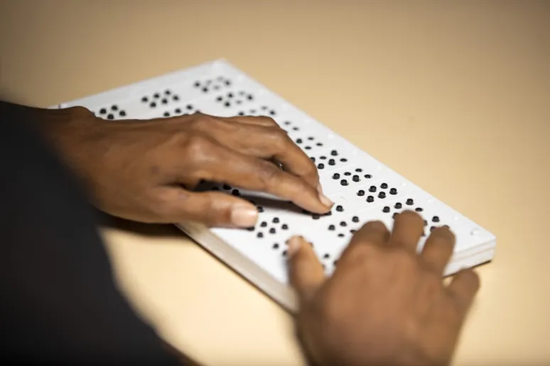 Two hands using a braille board.