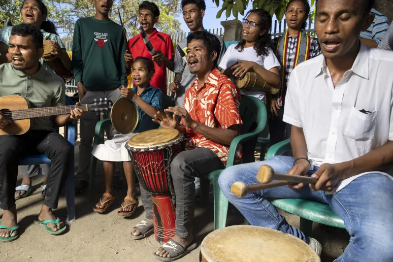 A group of people seated and standing, playing different musical instruments and singing.