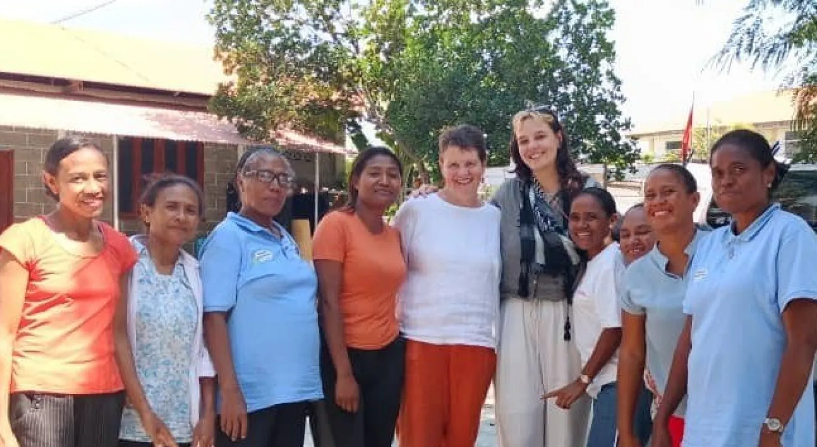 A group of nine people, all smiling at the camera, in an outdoor setting.