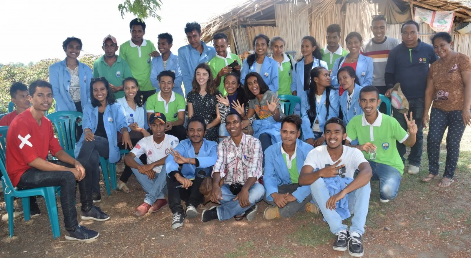 A group of people with blue and green shirts posing for the camera in an outdoor setting.