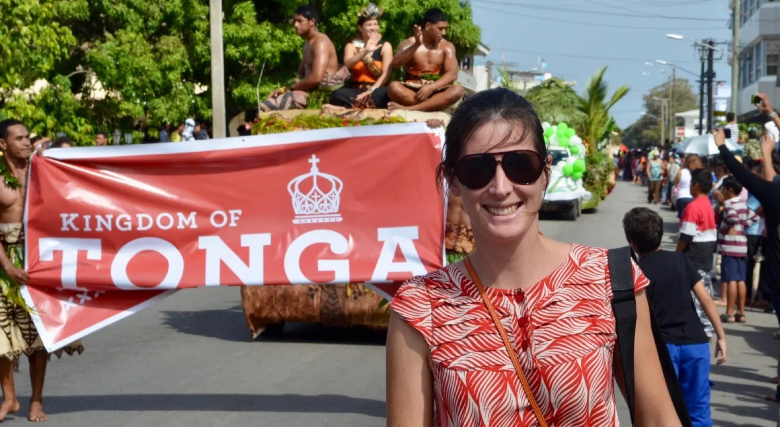 A person standing in front of a parade float in a street with a sign that says 'Tonga'.