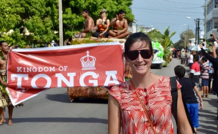 A person standing in front of a parade float in a street with a sign that says 'Tonga'.