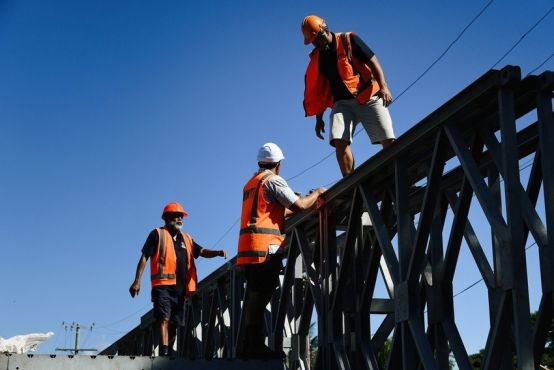 Three men in safety vests and hard hats work on scaffolding