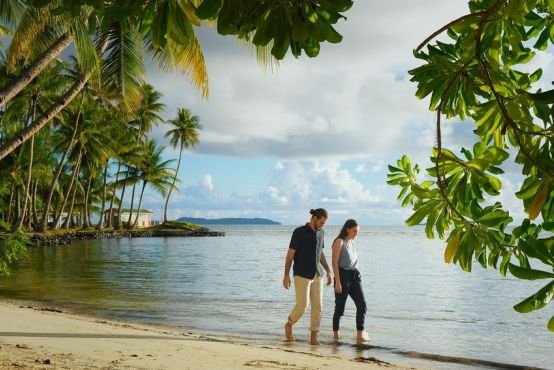 A man and a woman walk down a tropical beach holding hands
